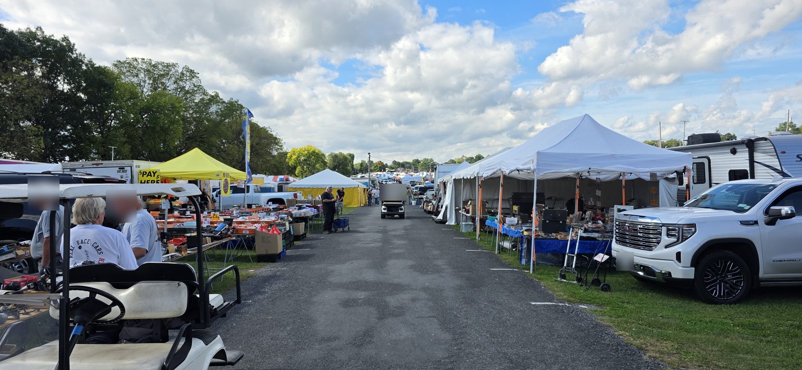 A long vendor aisle at Fall Carlisle on opening day: parts tables and white tents down both sides, with a golf cart parked in the foreground.